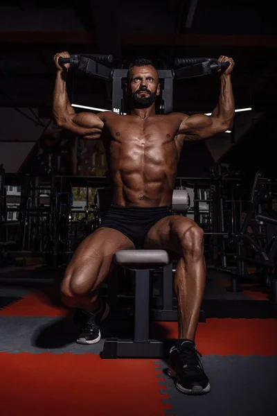 Hombre guapo con grandes músculos ejercitándose en el gimnasio. Muscular culturista haciendo ejercicios . — Foto de Stock