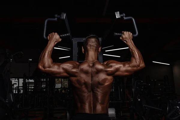 Hombre guapo con grandes músculos ejercitándose en el gimnasio. Muscular culturista haciendo ejercicios . — Foto de Stock
