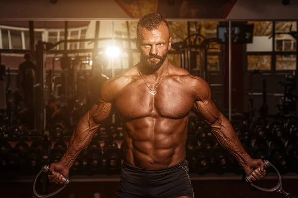 Hombre guapo con grandes músculos ejercitándose en el gimnasio. Muscular culturista haciendo ejercicios . —  Fotos de Stock