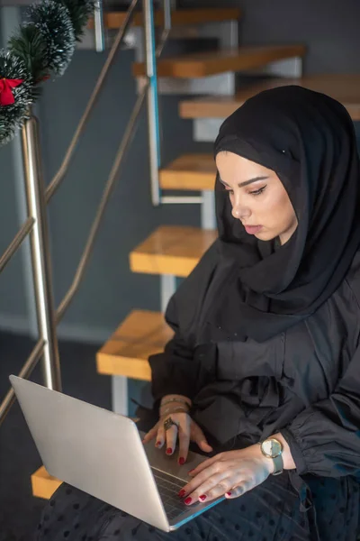Beautiful girl with hijab typing on laptop, speak on phone and learning about photography