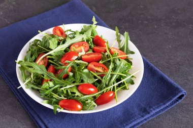Taze yeşil roka salatası ve beyaz seramik kasede domates kirazı..
