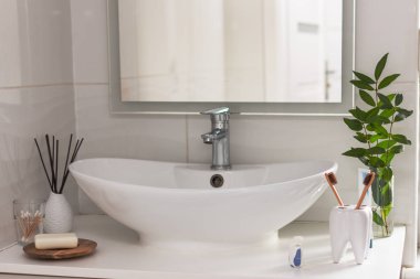 Banyo beyaz iç tarafında, diş şeklindeki bir bardakta biyolojik olarak çözünebilir, gübrelenebilir bambu diş fırçaları. Arkaplanda yeşil bitki dekoru.