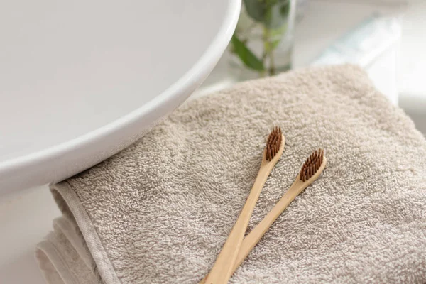 Due spazzolini di bambù biodegradabili e compostabili su un asciugamano in un bagno interno bianco. Decorazione vegetale verde sullo sfondo . — Foto Stock