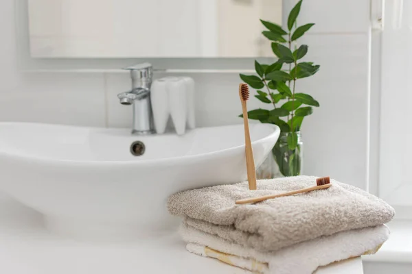 两个可生物降解的、可混合的竹子牙刷在浴室白色内壁的毛巾上。 背景中的绿色植物装饰. — 图库照片