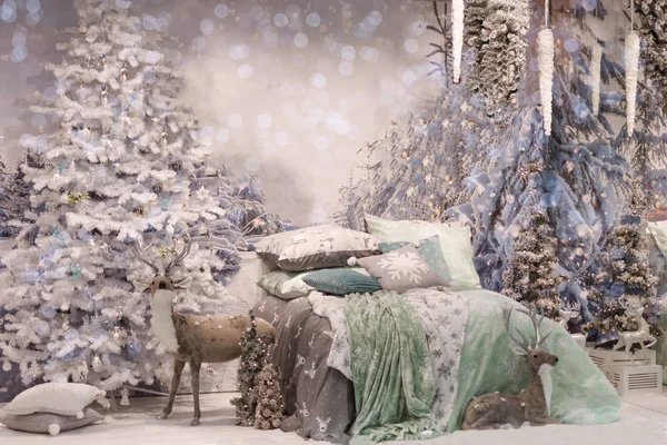 Acogedor dormitorio interior decorado con detalles de Navidad: juguete ciervo suave, árbol de Navidad, ramas en la pared cerca de la cama con nieve . — Foto de Stock