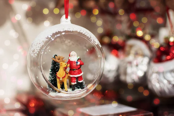 Kerstbal met de Kerstman en herten binnen over een heldere achtergrond met kleurrijke bokeh. Wintervakantie lichte decoratie. — Stockfoto