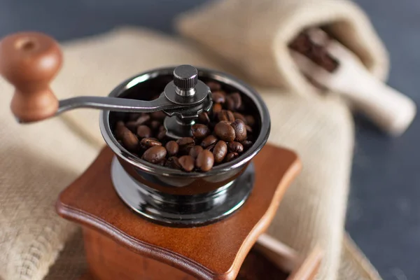 Ручная ручная кофемолка и кофейные зерна в мешочке из мешочка на деревянном столе . — стоковое фото