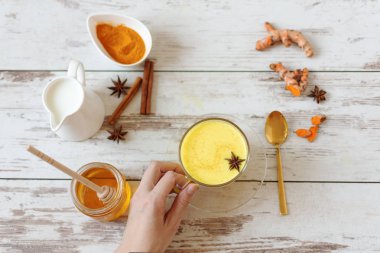 Kadın elinde tarçınlı ve diğer aromatik baharatlarla altın bir zerdeçal sütü tutuyor. Sağlıklı ve aromatik detoks içeceği. Bitkisel ilaçlar, iltihap önleyici tedaviler..