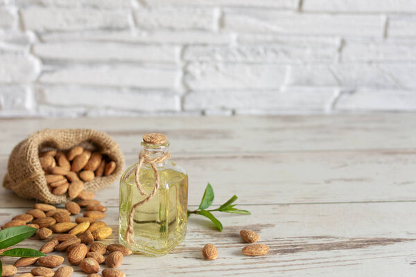 Almond oil in bottle and almond nuts on wooden background.