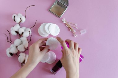 Pembe arka planda kadın eli ve kozmetik malzemeleriyle makyaj malzemesi çıkarmak için pamuk pedler..