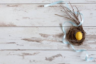 Sarı Paskalya yumurtası yaratıcı bir yuvada tahta masa manzaralı kurdeleli. Mutlu Paskalyalar.