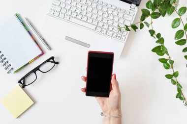 Ofiste cep telefonu kullanan kadın eli ile beyaz renkli modern işyeri.