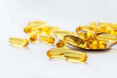 Morina ciğeri yağı omega 3 jel kapsülleri beyaz arka planda kaşık üzerinde.