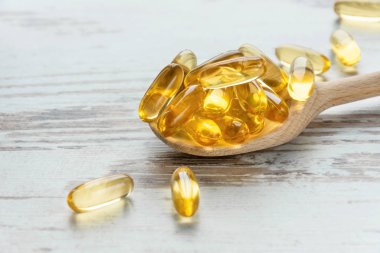 Morina ciğeri yağı omega 3 jel kapsülleri tahta arka planda kaşık üzerinde.