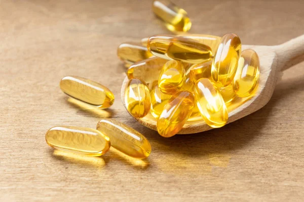 Morina ciğeri yağı omega 3 jel kapsülleri tahta arka planda kaşık üzerinde.
