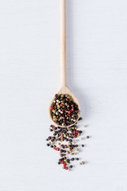 Tahta kaşıkta beyaz ahşap arka planda çok renkli biber tohumları.