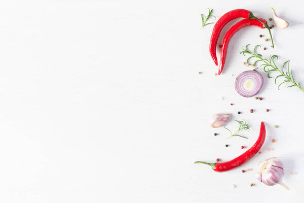 Composition of colorful pepper seeds, fresh chili pepper, garlic, blue onion and rosemary herb top view on white wooden background.