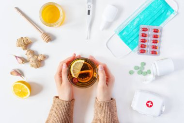 Soğuk algınlığı ve grip tedavilerinin bileşimi. Kadın eli sıcak çay tutuyor ve etrafında farklı tedaviler uyguluyor. Medicaments ve bitkisel tıp konsepti.