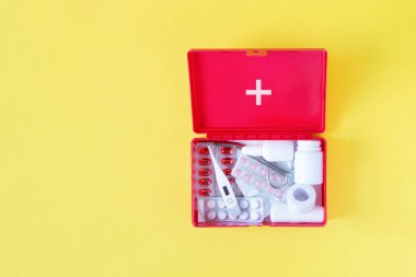 First aid kit red box with medical equipment and medications for emergency top view on pastel yellow background. clipart