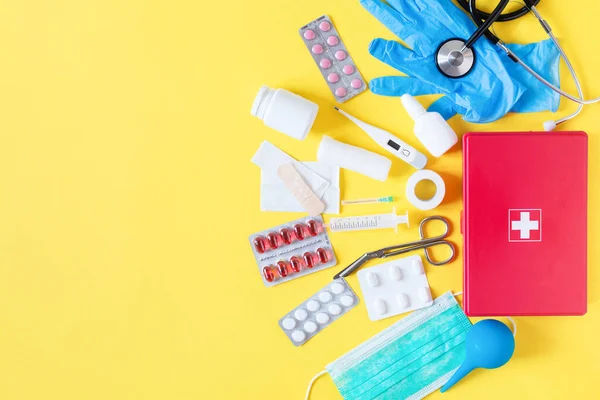 Красная коробка с медицинским оборудованием и лекарствами для экстренного просмотра сверху на пастельно-желтом фоне . — стоковое фото