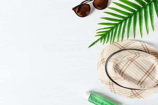 Summer composition with straw hat, sunglasses, palm leaf and sun protection oil on white wooden background top view. Summer fashion, vacation concept.