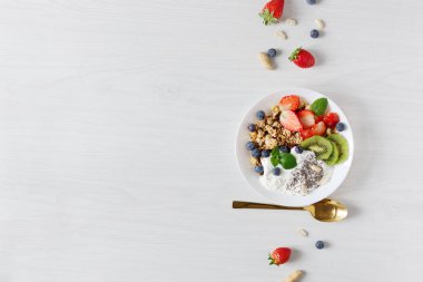 Beyaz seramik kase ev yapımı granola yoğurt, taze böğürtlen ve beyaz ahşap masa üstü manzaralı meyveler. Uzayı kopyala Sağlıklı yeme kavramı.