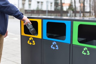 Plastik atık için çöp kutusuna plastik şişe atan adamın eli. Ayrı çöpler için modern renkli çöp kutuları. Çevresel bilinç yaşam tarzı.