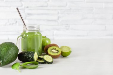 Tuğla duvarın üzerinde beyaz ahşap masada yeşil meyve ve sebzeler. Detoks diyeti. Sağlıklı yeme kavramı.