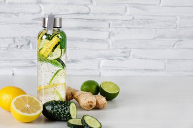 Detoks suyu limon, kireç, zencefil ve salatalık ile doldurdu. Beyaz ahşap arka planda, tuğla duvarın üzerinde cam bir spor şişesinde. Detoksifikasyon. Sağlıklı yeme kavramı.