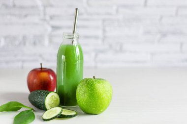 Yeşil ve kırmızı elmadan yapılmış bir şişe detoks yeşili smoothie, beyaz ahşap masada ıspanak ve salatalık. Süper yiyecek, sağlıklı yeme konsepti.