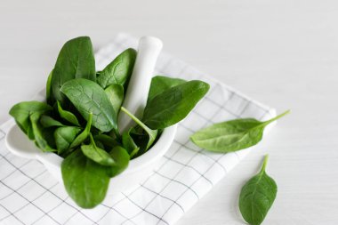 Beyaz ahşap masada, fani kasede yeşil ıspanak yaprakları. Sağlıklı beslenme konsepti. Detoksifikasyon.