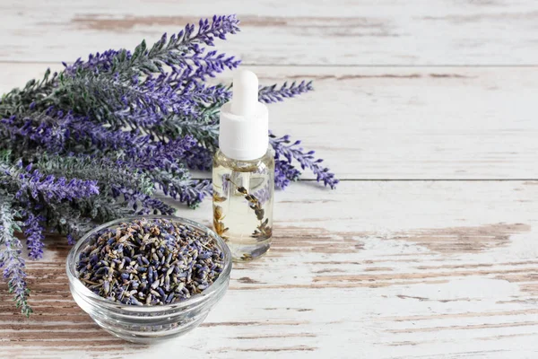 Bunch of lavender flowers, dried lavender and aromatic lavender oil on white wooden background. Copy space.