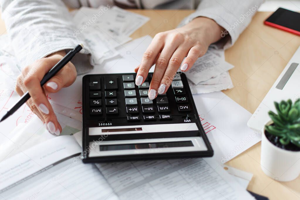 Woman holding bills and calculating them. Workplace with computer, calculator, smartphone and documents. Payment concept.