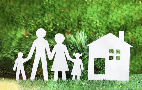 White paper cut of family with house on green grass background. Happy family concept.