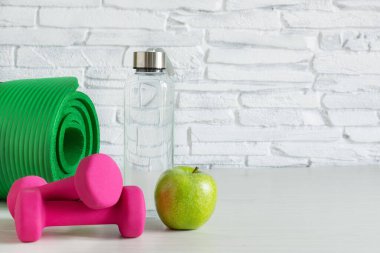 Pembe dambıllar, bir şişe su ve beyaz ahşap masada yeşil elma. Sağlıklı yaşam tarzı kavramı. Spor haberleri. Boşluğu kopyala.