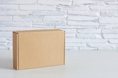Beyaz tuğla duvarın yanında beyaz ahşap arka planda karton kutuda. Teslimat konsepti. Boşluğu kopyala.