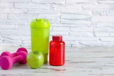 Protein haplı kompozisyon, yeşil karıştırıcı ve beyaz ahşap arka planda pembe dambıllar. Spor içeceği konsepti.