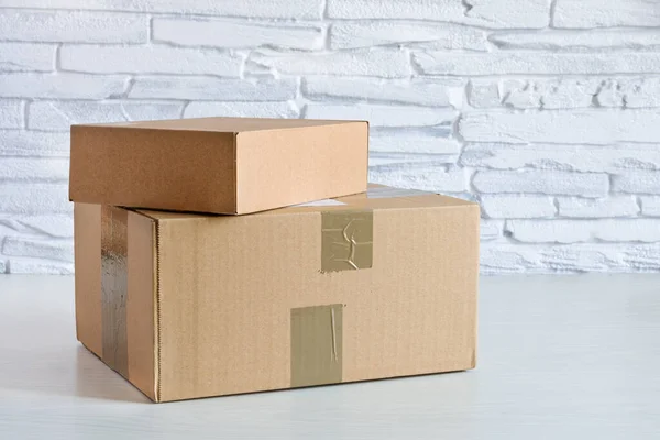 Parcel in cardboard box on white wooden background near white brick wall. Delivery concept. Copy space.