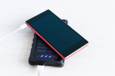 Beyaz ahşap arka planda güneş pili paneline bağlı akıllı telefon. Kablosuz cep telefonu şarj cihazı.