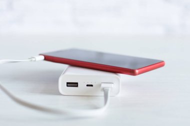 Beyaz ahşap arka planda elektrik bankasıyla çalışan akıllı telefon. Kablosuz şarj cihazı..