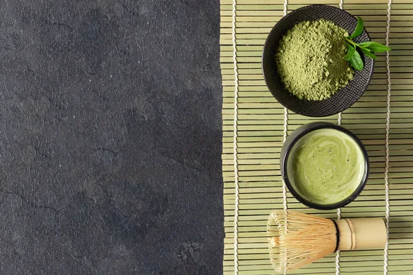 Green matcha tea drink and tea accessories on black background top view. Japanese tea ceremony concept. Chashaku spoon and chasen bamboo whisk for brewing matcha tea.