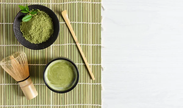 Organic green matcha tea and tea accessories on japanese mat on white wooden background. Japanese tea ceremony concept. Chashaku spoon and chasen bamboo whisk for brewing matcha tea.