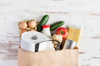 Çeşitli yiyeceklerle dolu kağıt alışveriş torbası. Yiyecek bağışı, güvenli teslimat hizmeti konsepti. Makarna, yumurta, konserve yiyecek, bir şişe yağ ve süt alışveriş poşetinde..