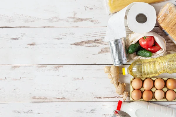 Various food products such as pasta, eggs, canned food, bottle of milk and oil top view on wooden background. Food donation, safe delivery service concept. Grocery shopping.