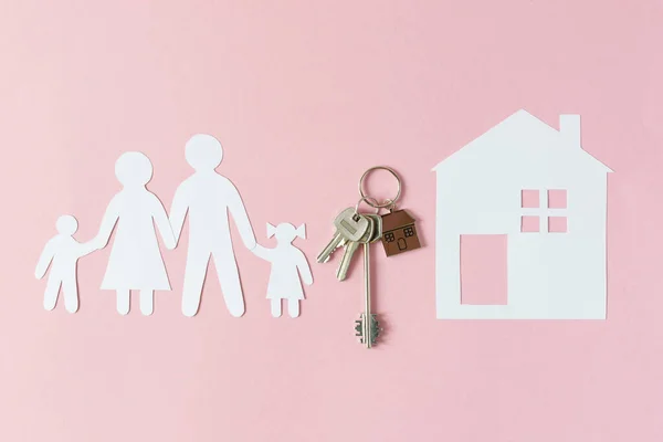 Composition with paper family cutout and paper house with key and keychain in a house shape top view on pink bakground. Buying house concept.