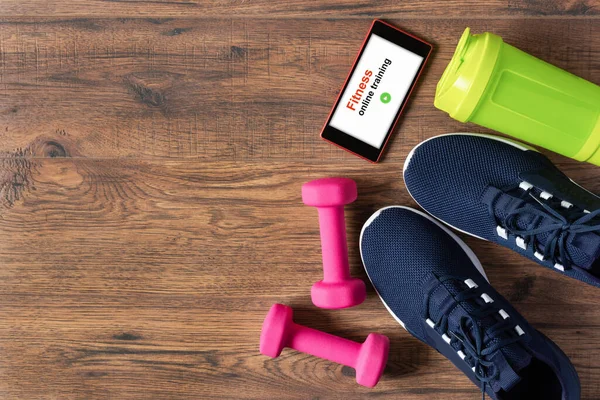 Spor aletleri, spor ayakkabıları ve ahşap arka planda akıllı telefon. Spor eğitimi için kapalı alanda uygulama. Çevrimiçi Fitness eğitimi konsepti. Evde kalarak online egzersiz yapıyorum..