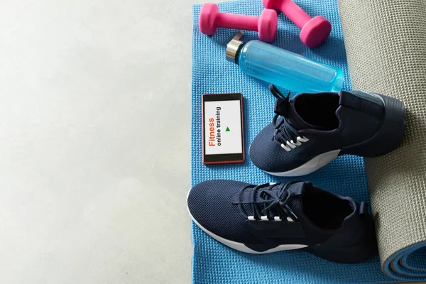 Fitness equipment and smartphone on gray floor background. Training indoors. Home online workout.