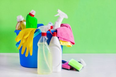 Bir kova dolusu deterjan ve yeşil arka planda temizlik aletleri. Ev işi temizlik konsepti.
