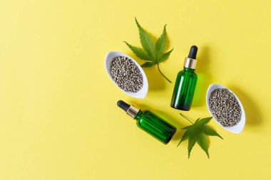 CBD yağlı cam şişeler, kuru ve taze kenevir yaprakları, sarı arka plan manzaralı kenevir tohumları. Alternatif tıp konsepti. Bitkisel kozmetik.