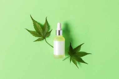 Yeşil arka planda tıbbi CBD yağlı cam şişe ve taze kenevir yaprakları. Alternatif tıp konsepti. Bitkisel kozmetik.